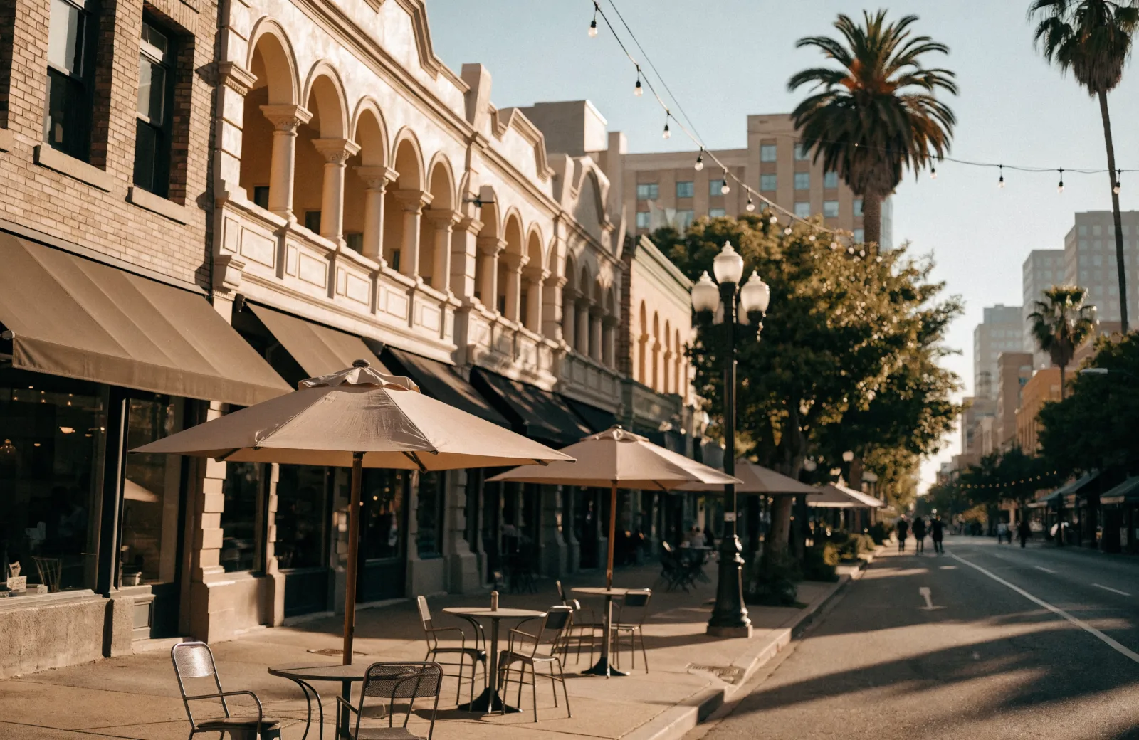 Sidewalk cafe tables under umbrellas along a sunny downtown Palo Alto shopping street at golden hour